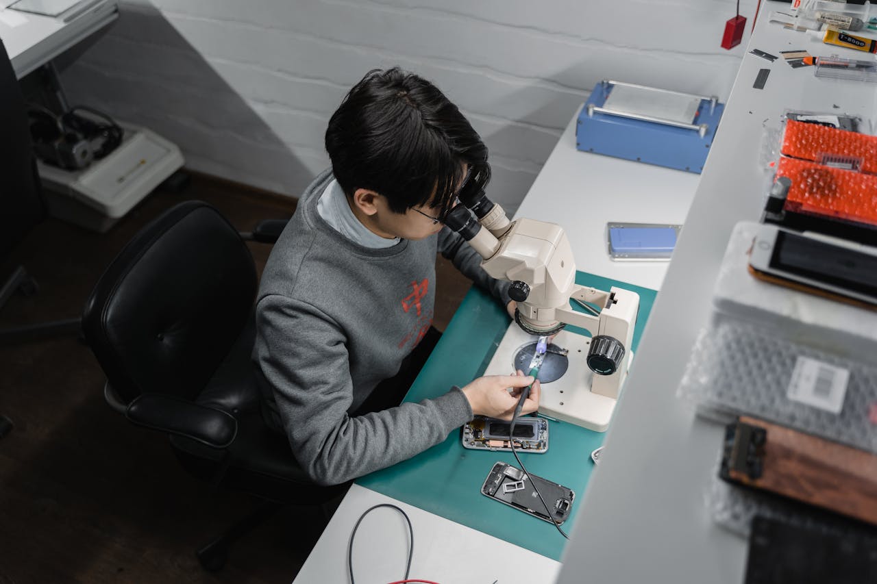 about-us Technician works on smartphone repair under a microscope, indoors at a tech bench.
