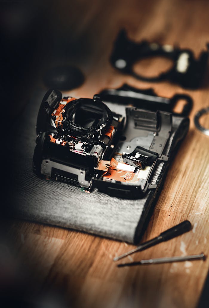 services-02 Detailed view of a disassembled camera on a table, showcasing repair tools and parts.
